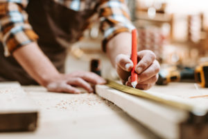 cropped view of man holding pencil near wooden plank and measuring tape